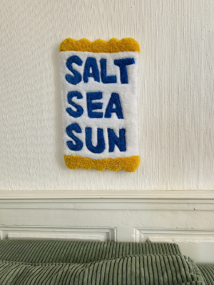 Tapis mural en tufting avec l'inscription 'Salt, Sea, Sun', aux tons bleus et jaunes, fabriqué en laine acrylique avec finition antidérapante.